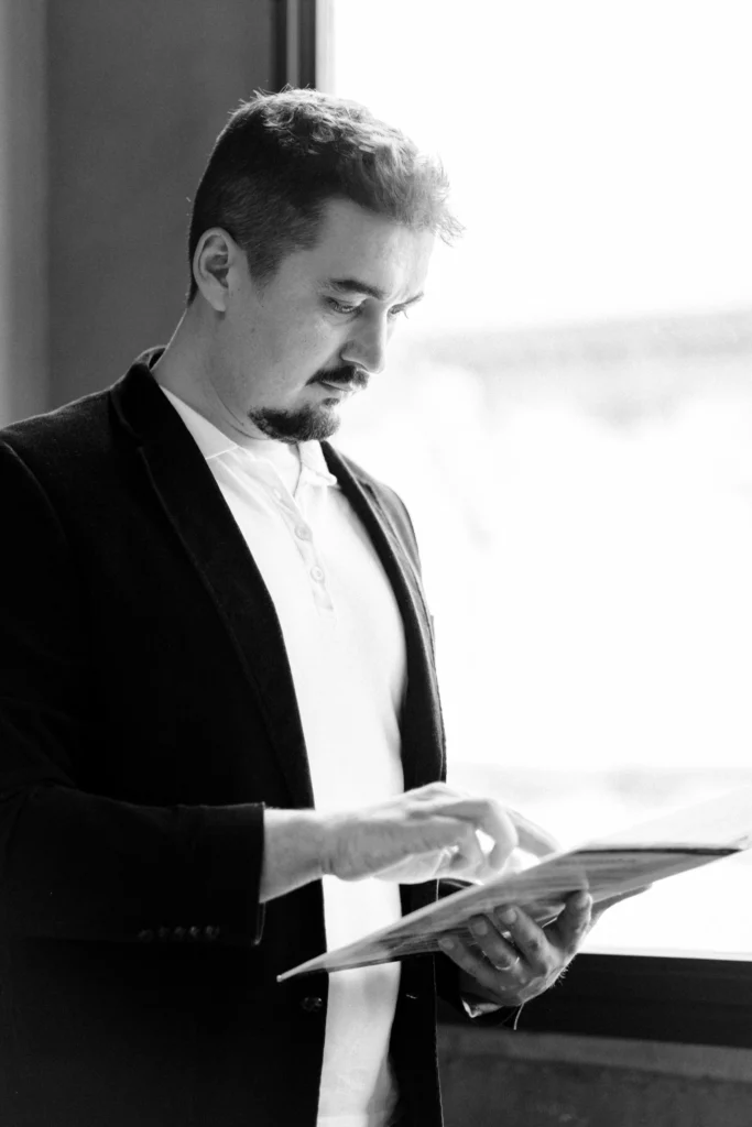 Kristian Selimi - Fondatore di Valutenze.it Kristian Selimi in piedi, leggendo un documento, vestito in modo professionale.